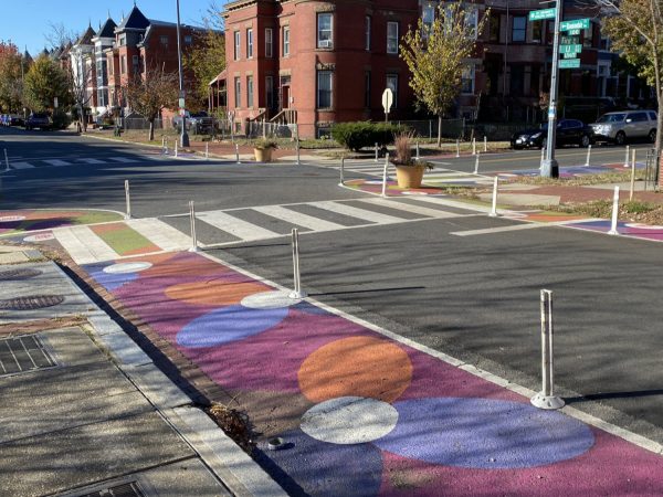 A Washington, DC intersection with a painted daylight zone of colorful circles, flexible posts, and a planter beside the crosswalk.